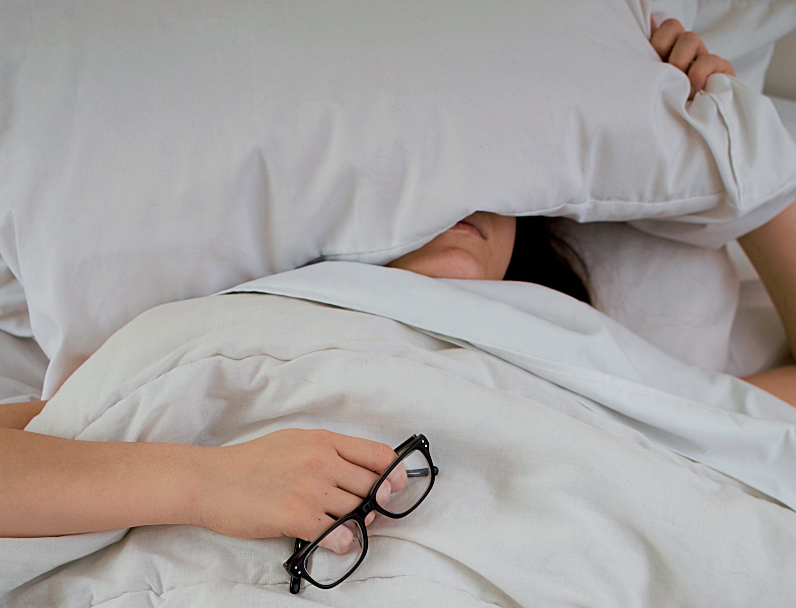 femme au lit avec ses lunettes et un coussin sur la tête